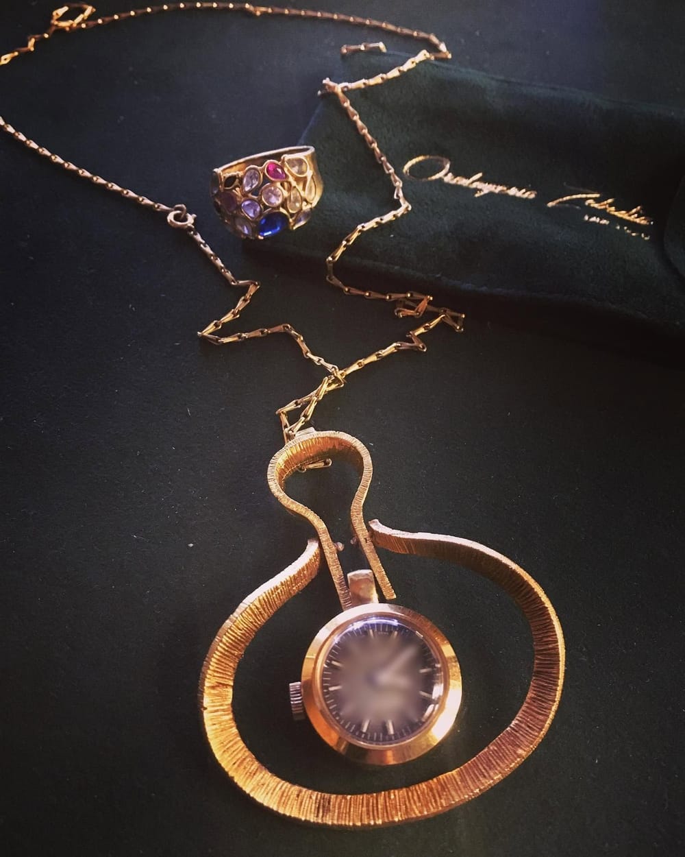 Una monachina da collo in oro con la catena, accanto un anello con le pietre.