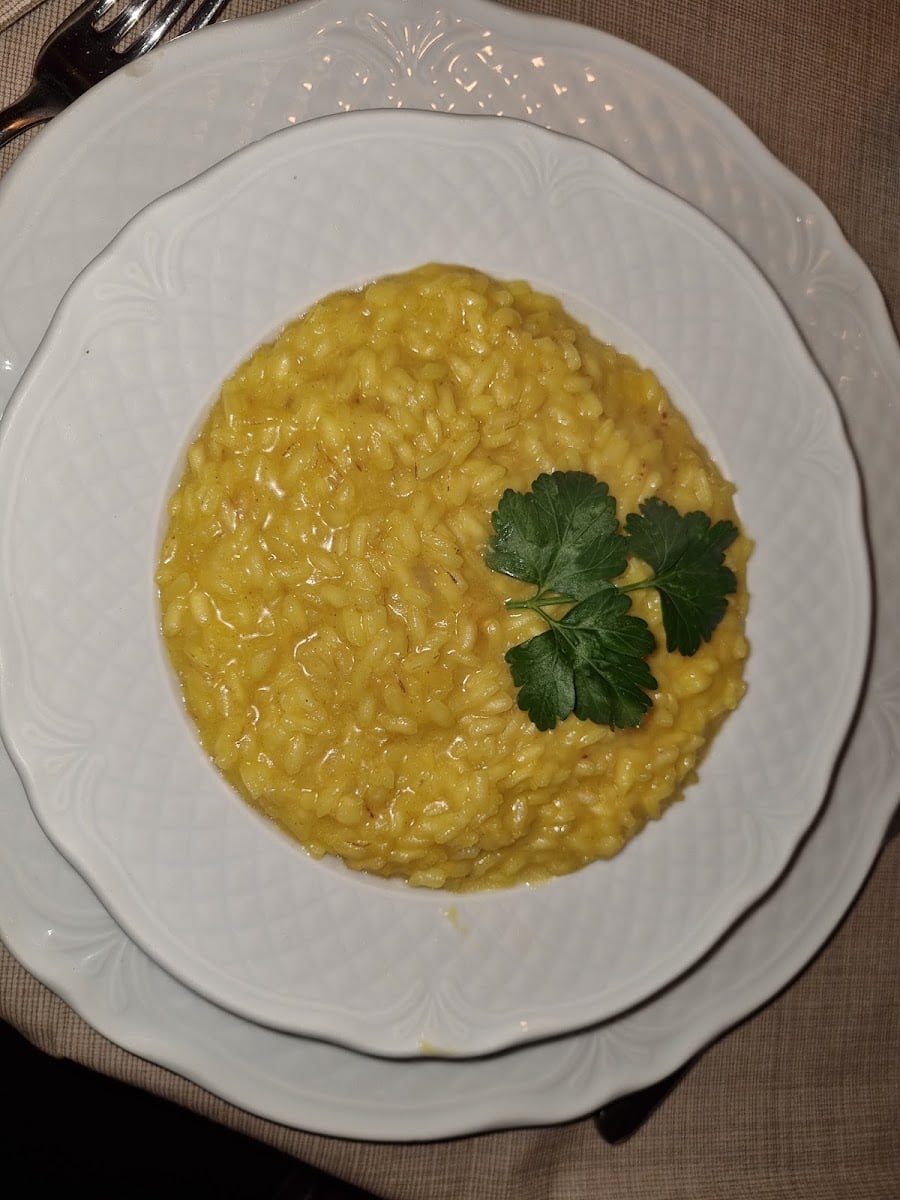 Risotto alla milanese giallo zafferano su piatto bianco lavorato, visto dall'alto