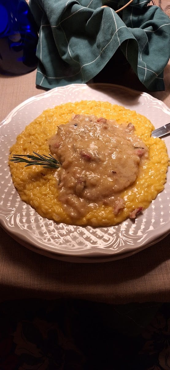 Risotto giallo con sopra un secondo di carne in salsa e un rametto di rosmarino