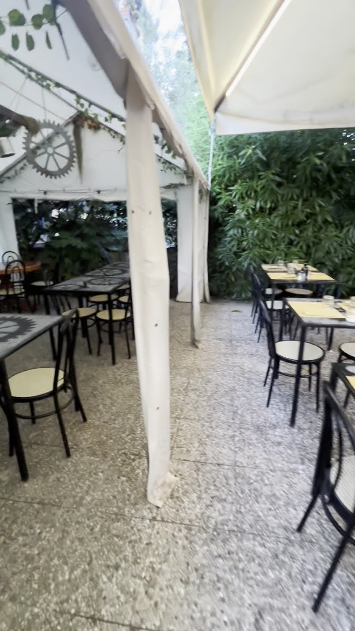 Il giardino interno: tavoli con il piano a mosaico, sedie nere, pergolato bianco e una siepe verde molto fitta
