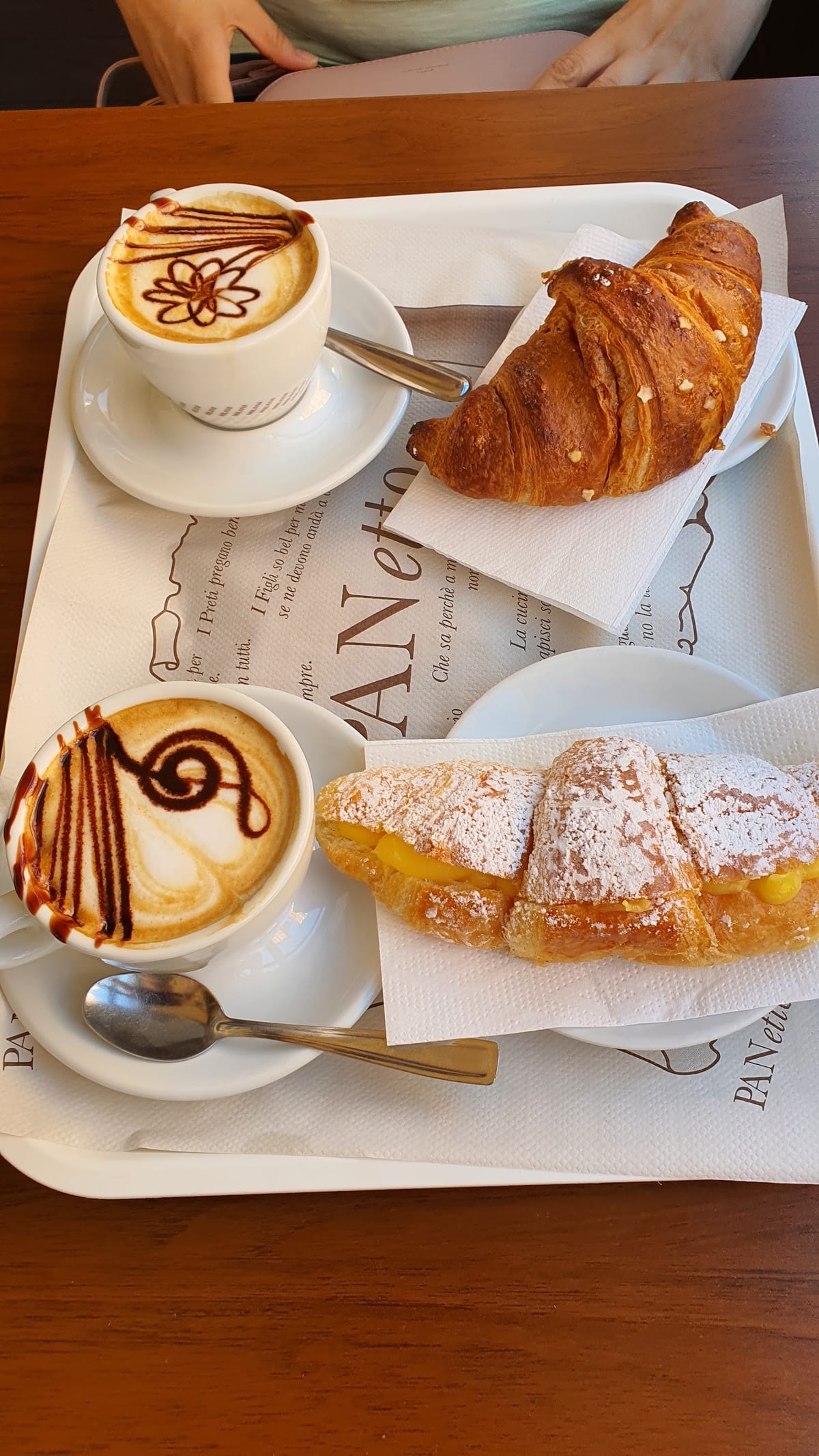 Vassoio con due cappuccini decorati, un cornetto e una brioche alla crema, sulla carta brandizzata PANetto