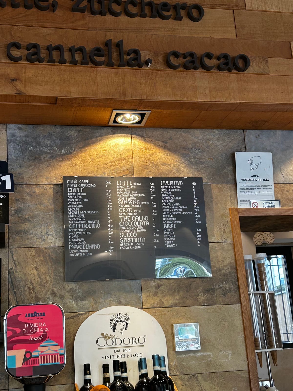 Il listino delle bevande appeso al muro del locale, sotto le lettere di legno latte zucchero cannella cacao
