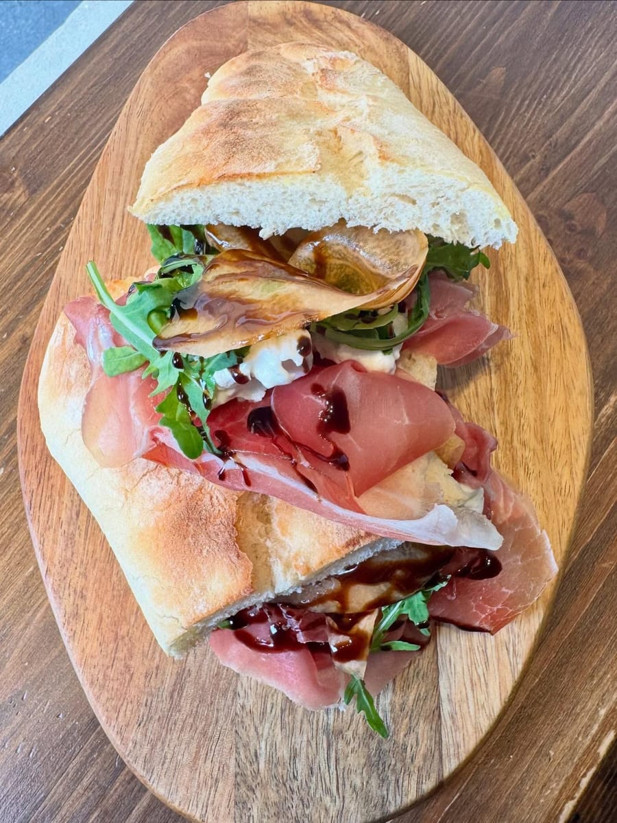 Crudo, rucola e glassa nel pane bianco, sul tagliere ovale.