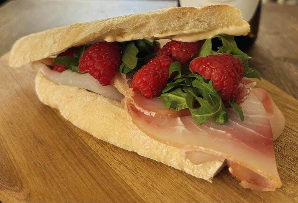 Crudo, lamponi e rucola nel pane bianco.