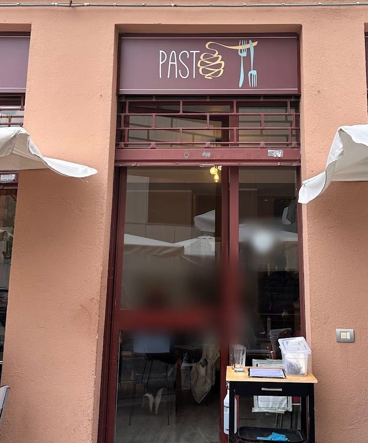 La facciata color salmone con l'insegna bordeaux «PASTO», la porta rossa e gli ombrelloni bianchi.