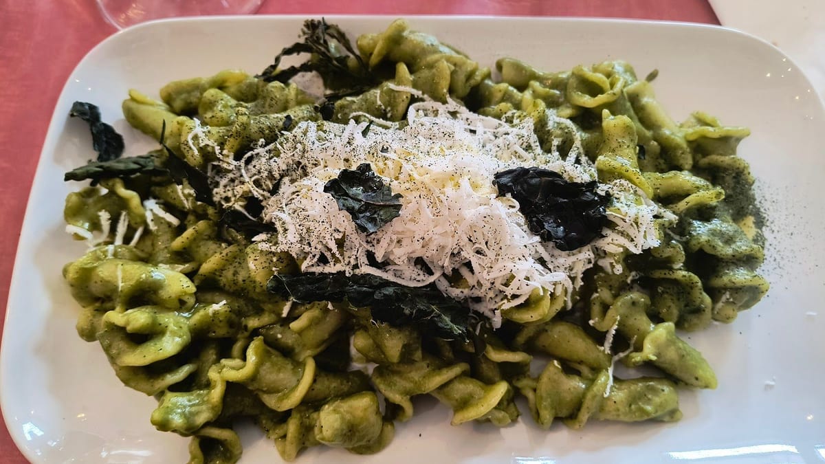 Un piatto di gigli al pesto con la burrata, sul tavolo rosso.