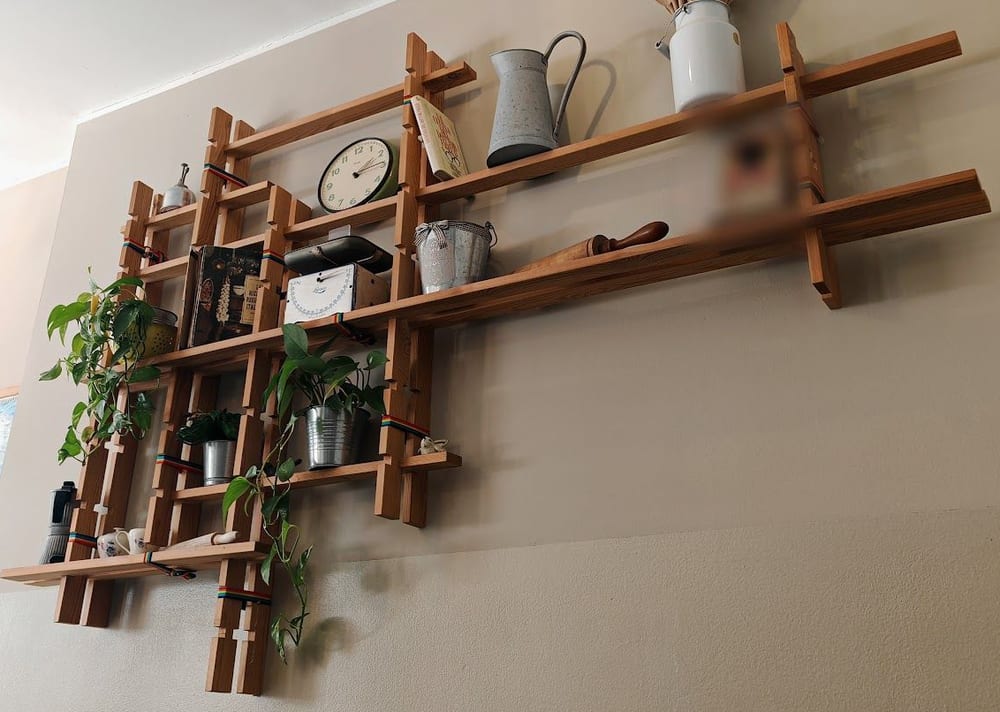 La parete della sala: le mensole di legno a incastro con l'orologio, le brocche di zinco, le piante e i cucchiai di legno.