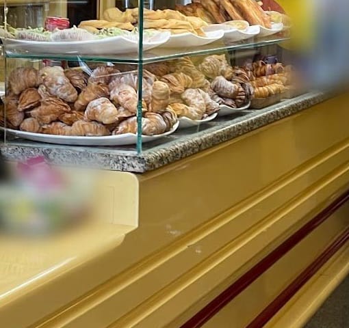 Il banco di legno laccato crema coi filetti rossi, il piano di granito e la vetrina coi cornetti.
