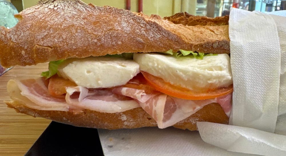 Un panino lungo col crudo, la mozzarella e il pomodoro, nella carta.