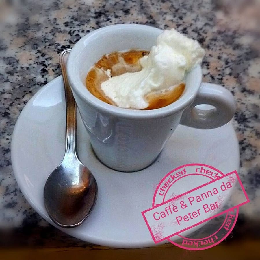 La tazzina sul granito con un cucchiaio di panna sopra il caffè, il cucchiaino sul piattino e il timbro rosa «Caffè & Panna da Peter Bar».