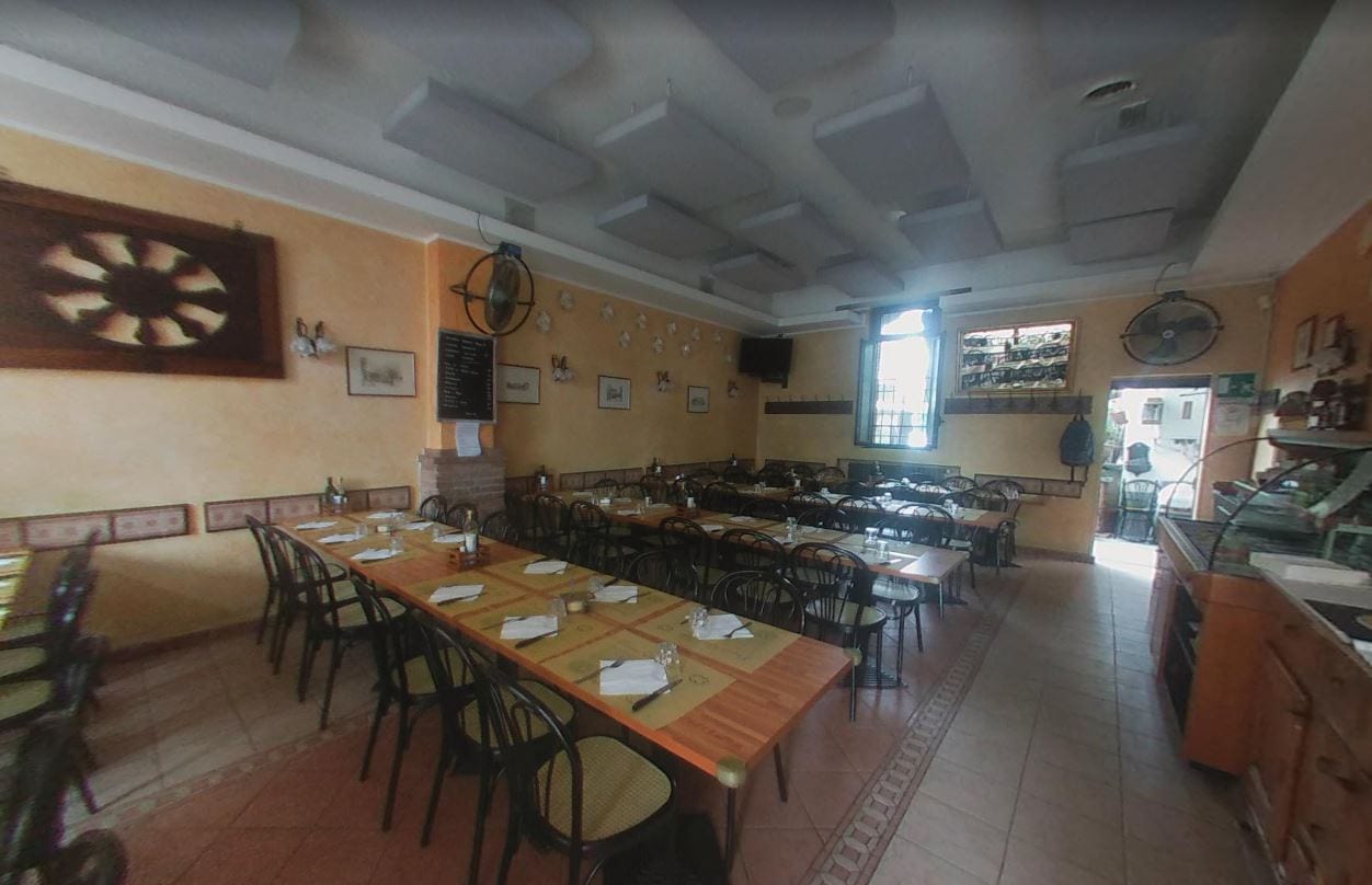 La sala del Quadrifoglio: lunghe tavolate con tovagliette gialle, sedie Thonet e la lavagna del menu