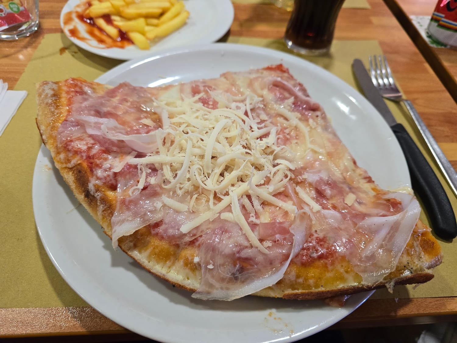 Trancio con prosciutto crudo e grana grattugiato, servito con un piatto di patatine fritte
