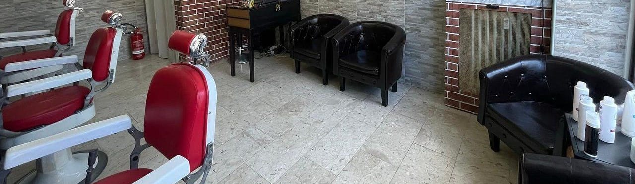 Tre poltrone da barbiere rosse e bianche e, in fondo, le due poltroncine nere dell'attesa e il muro di mattoni
