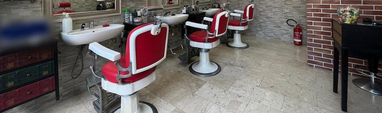 Le poltrone da barbiere rosse e bianche in fila davanti ai lavandini, sul pavimento di marmo chiaro