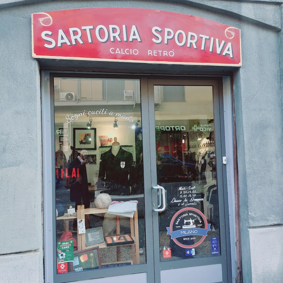 La vetrina in Via Ignazio Ciaia 6, con il claim «Sogni cuciti a mano» scritto sul vetro e lo stemma con la macchina da cucire