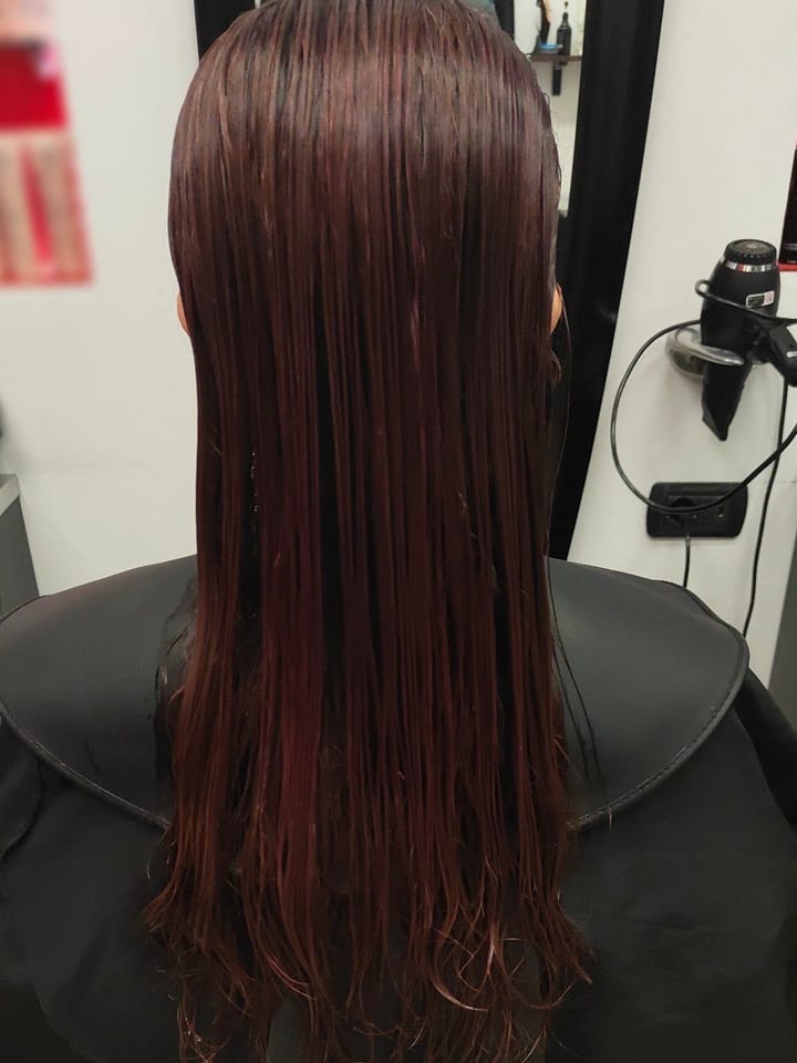Capelli lunghi e lisci color bordeaux, visti di spalle davanti allo specchio.