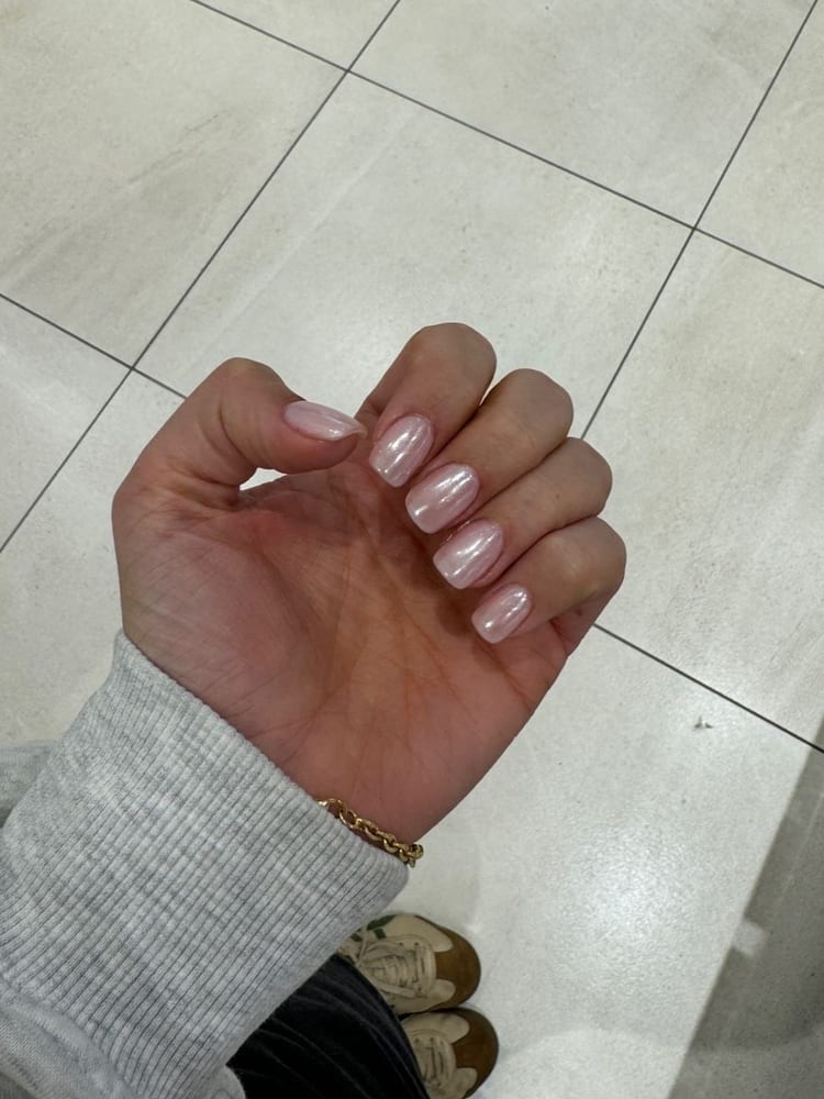 Unghie corte color perla, la mano chiusa sopra il pavimento chiaro.