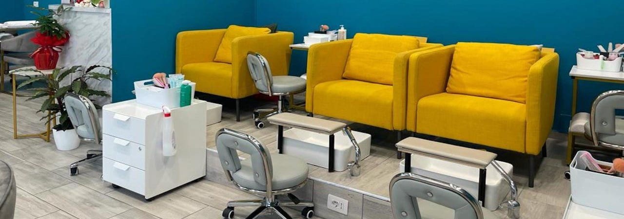 La fila delle poltrone senape della pedicure, coi poggiapiedi e gli sgabelli.