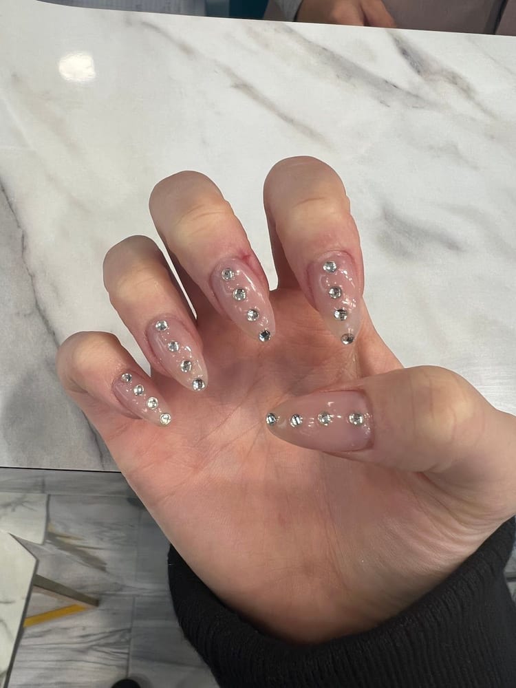 Unghie nude con piccoli brillantini, sul marmo bianco del tavolo.