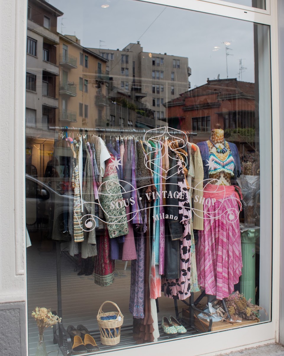 La vetrina di Sous Vintage Shop: il logo liberty inciso sul vetro, dietro un rack di abiti vintage colorati, un manichino e un cestino di vimini
