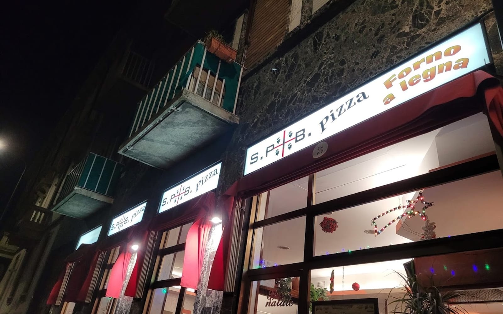 La facciata di Spib Pizza di sera, con l'insegna illuminata Forno a legna