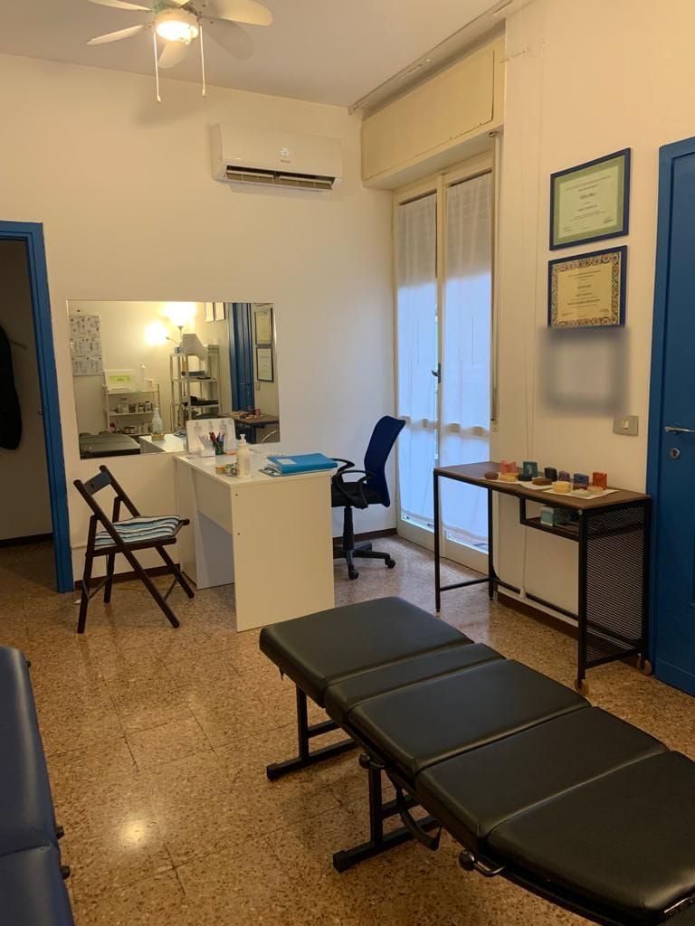 L'ingresso dello studio: la scrivania, la finestra, le porte blu e i diplomi alla parete; in primo piano un lettino.