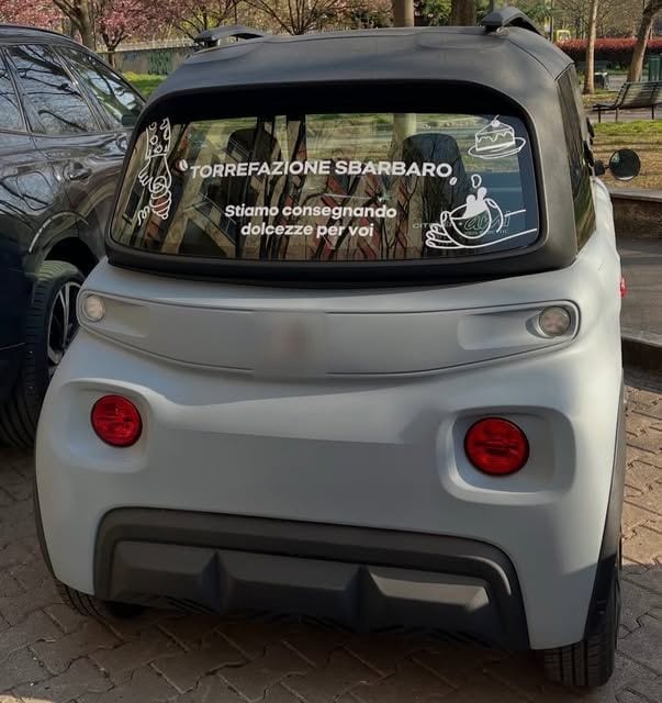 Una piccola auto grigia con la scritta «Torrefazione Sbarbaro · Stiamo consegnando dolcezze per voi» sul lunotto.