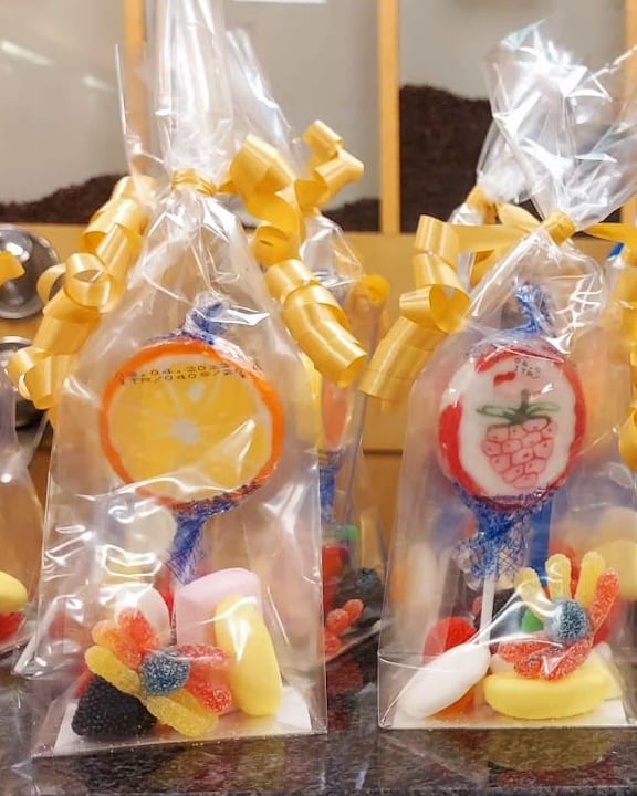 Una fila di sacchetti di cellophane sul banco di granito, ognuno col lecca-lecca a disco, le gelatine e il nastro dorato arricciato.