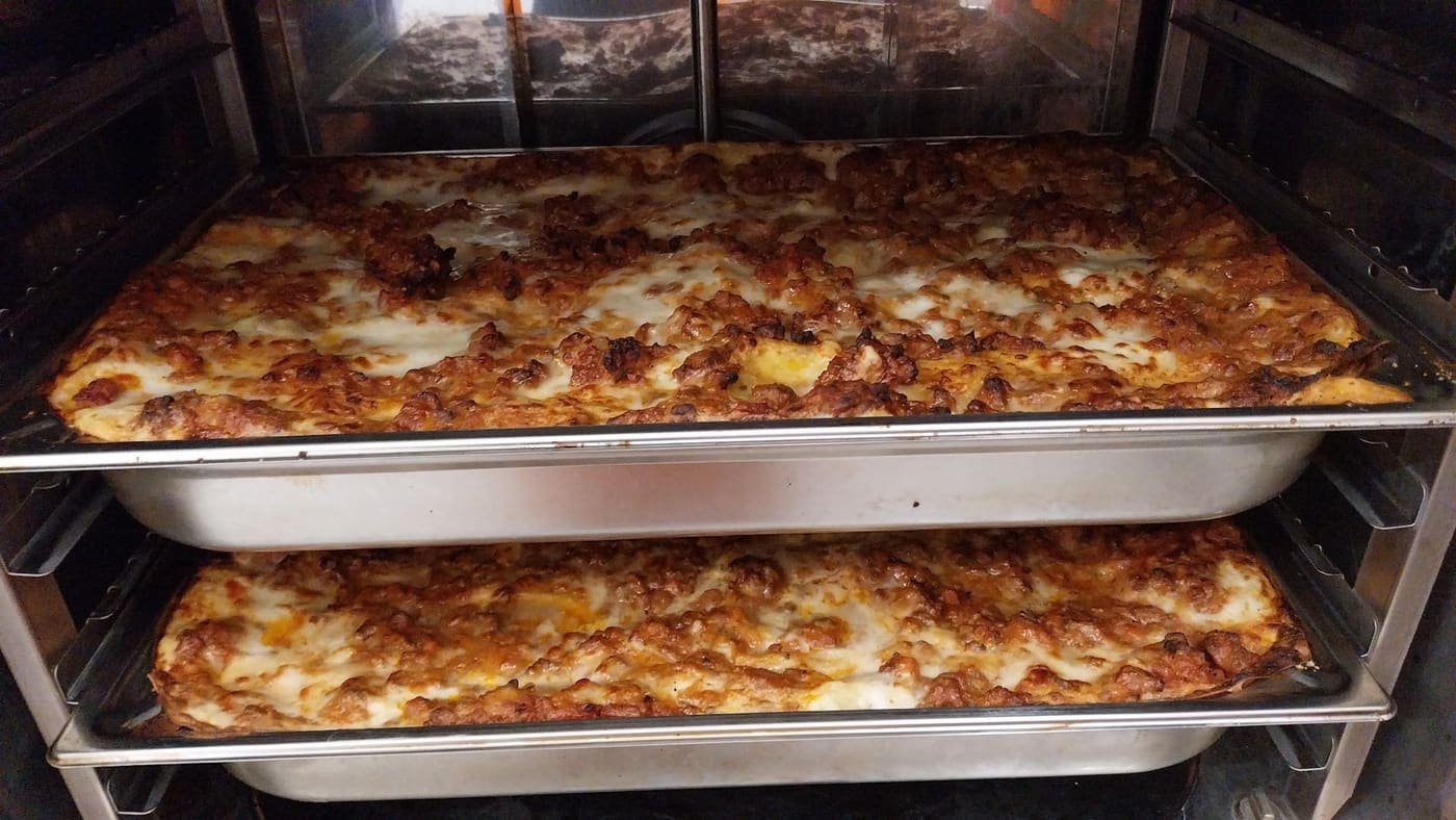 Due teglie di lasagne sulle griglie del forno.