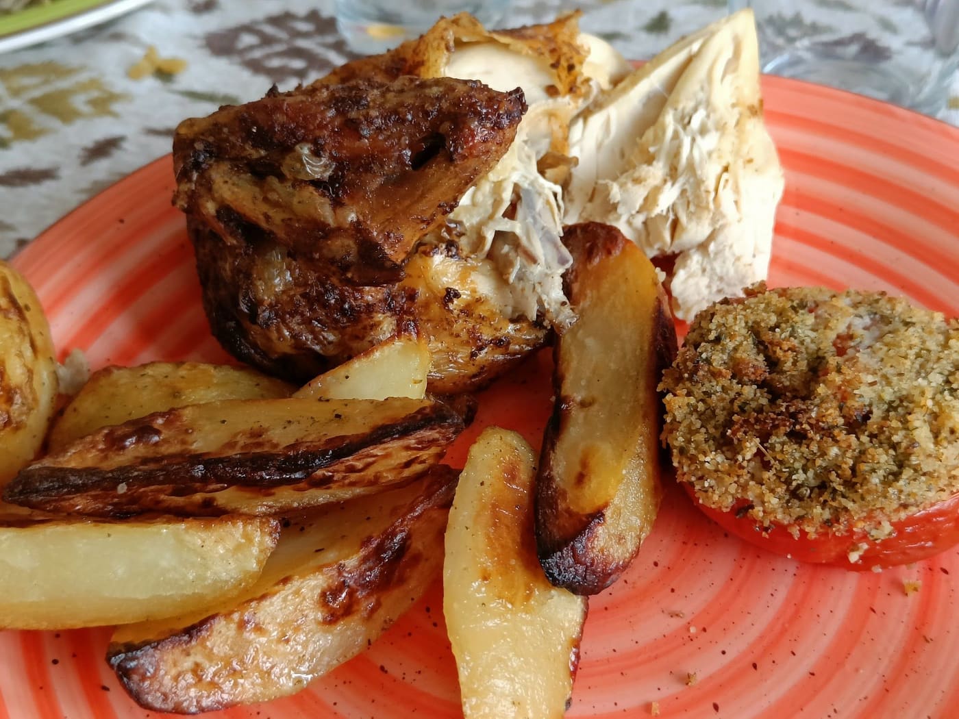 Un piatto col pollo, le patate al forno e il pomodoro ripieno.