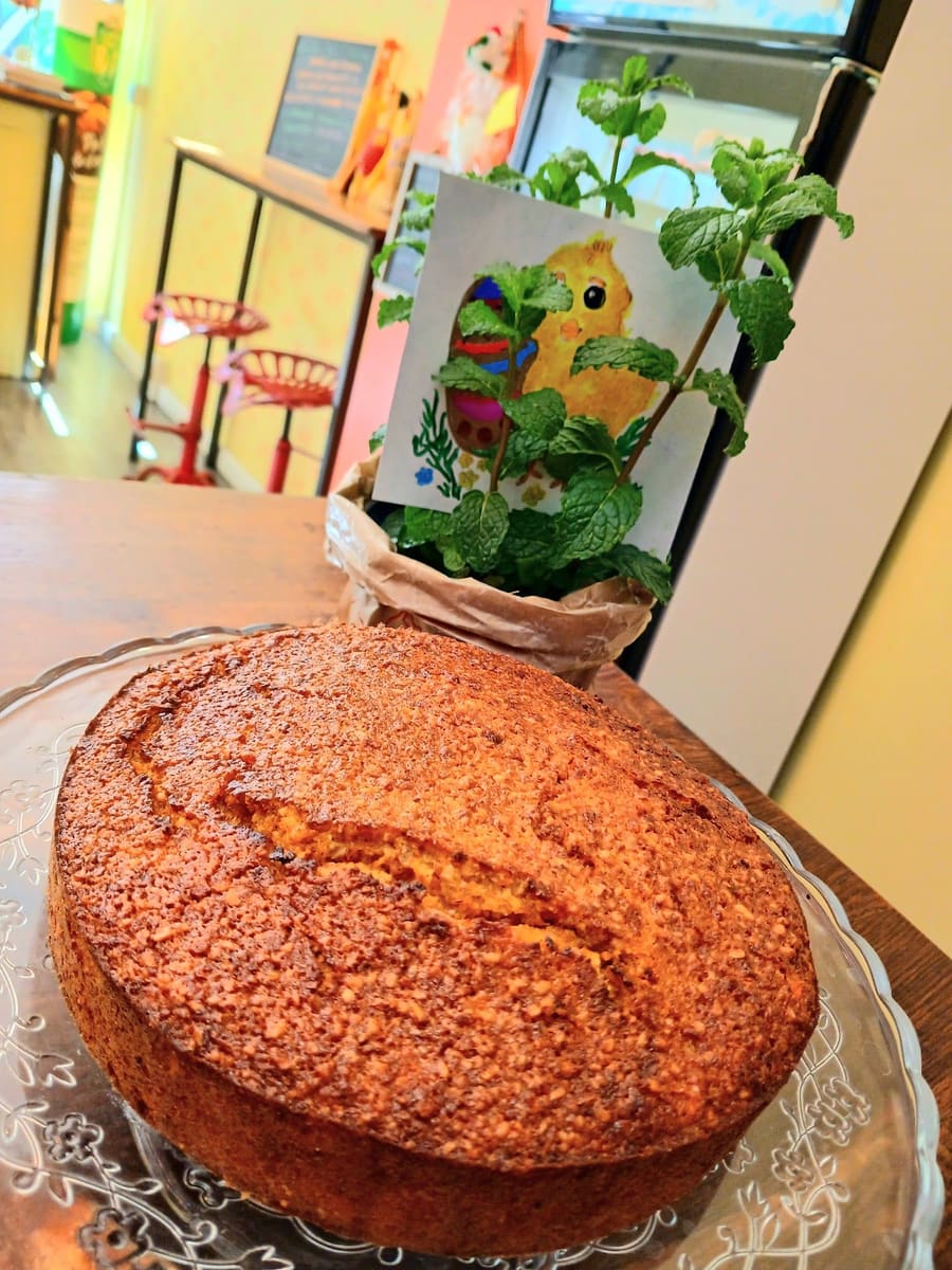 La torta sul piatto di vetro; dietro, il muro giallo e gli sgabelli rossi della bottega.