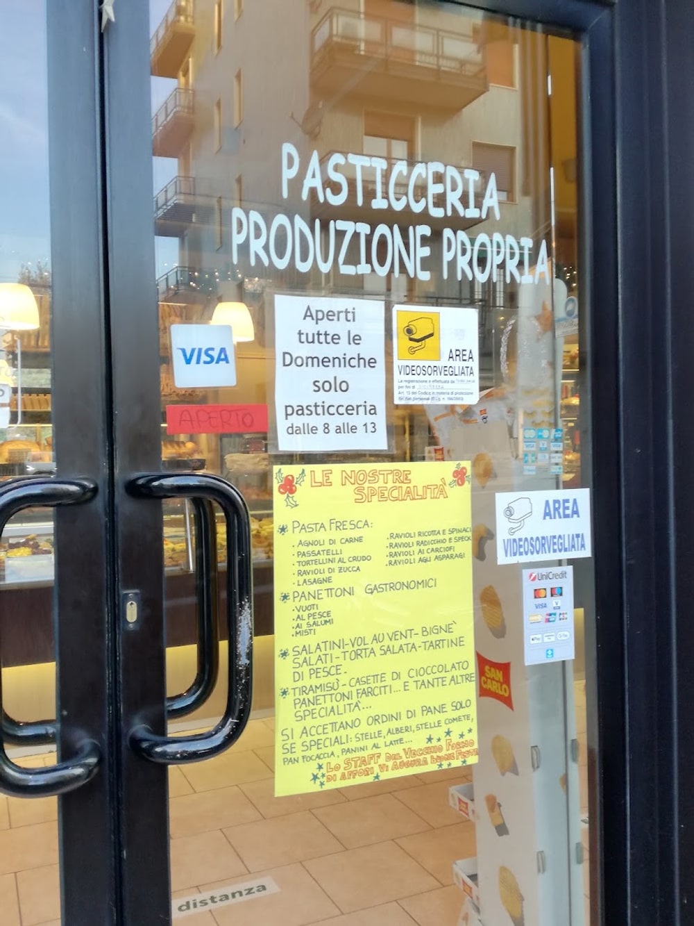 La porta del forno con «Pasticceria produzione propria» dipinto sul vetro e il cartello giallo delle specialità scritto a mano
