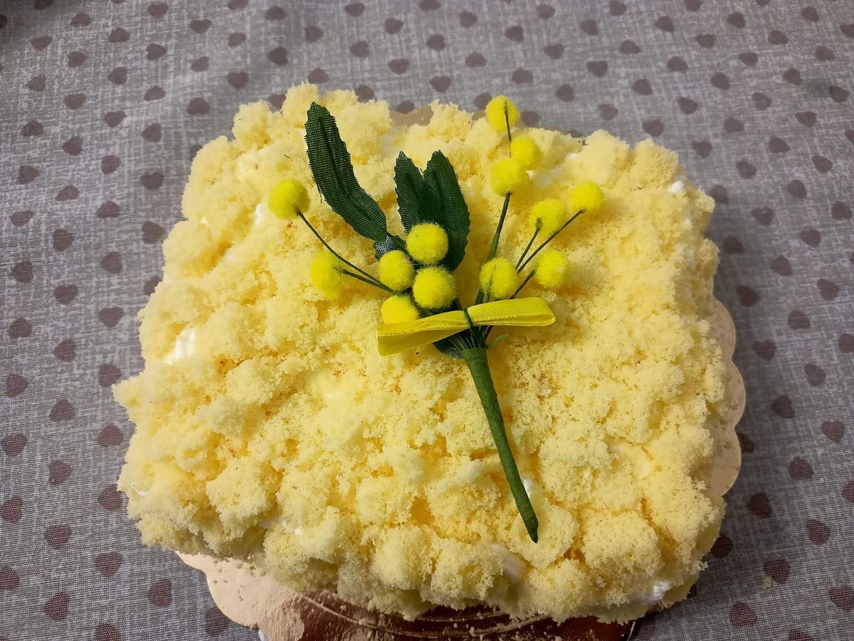 Torta Mimosa, coperta di pan di Spagna sbriciolato e decorata con un rametto di mimosa