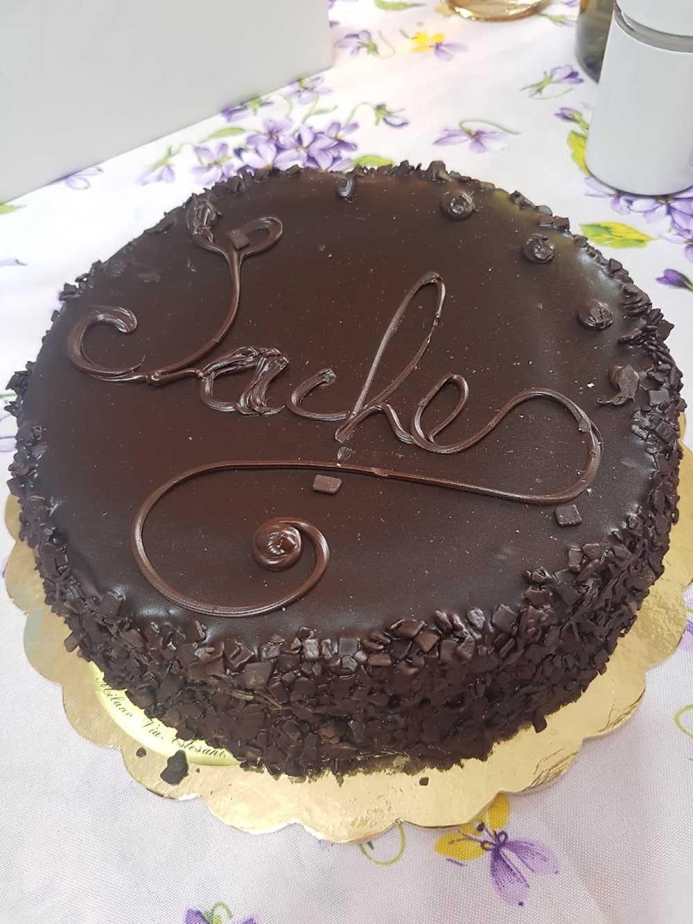 Torta Sacher con la scritta «Sacher» in cioccolato e scaglie tutto attorno