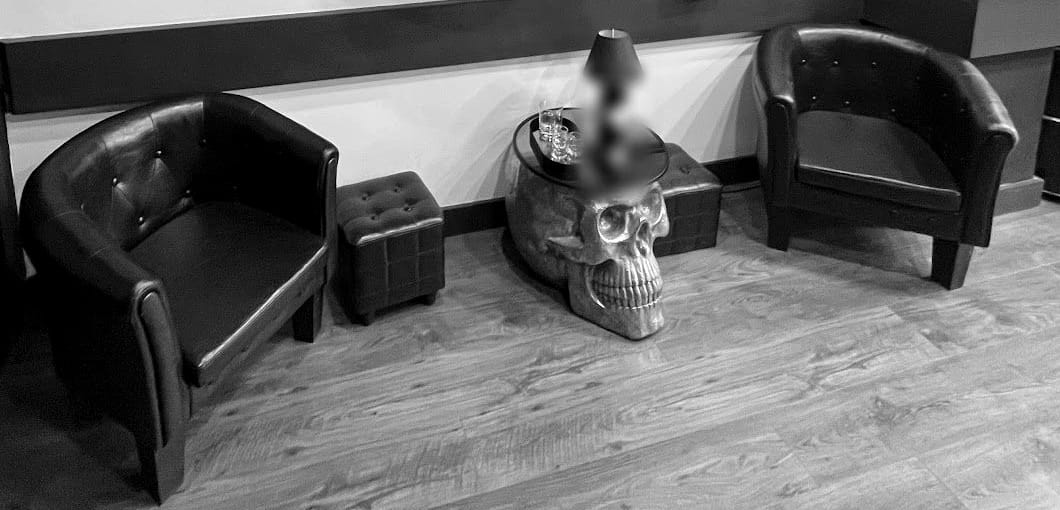 L'angolo d'attesa: due poltroncine di pelle scura, due pouf e un tavolino a forma di teschio dorato con una lampada