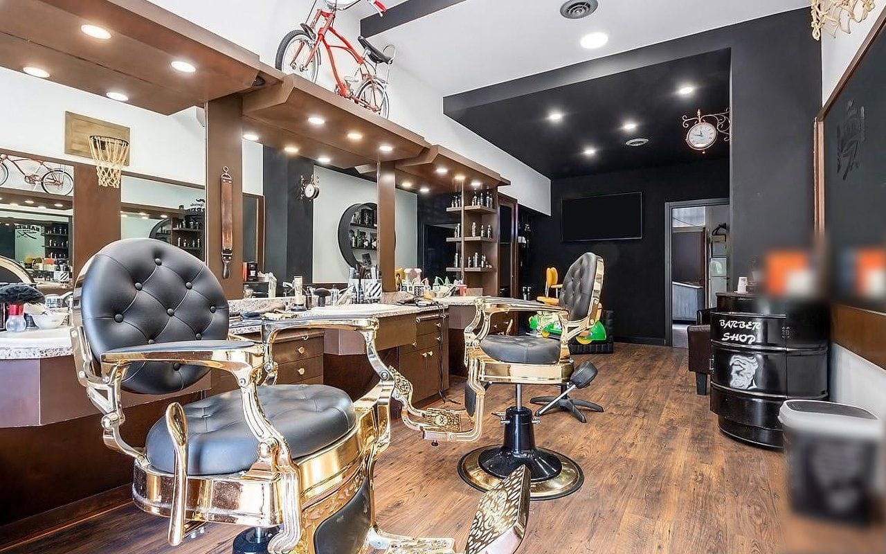 Il salone: le poltrone nere e oro, una bici chopper rossa sopra il mobile degli specchi, un canestro da basket, l'orologio da stazione sulla parete nera e un barile con la scritta Barber shop