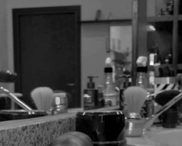 In bianco e nero: due pennelli da barba e le ciotole sul banco di granito, dietro lo specchio e le mensole